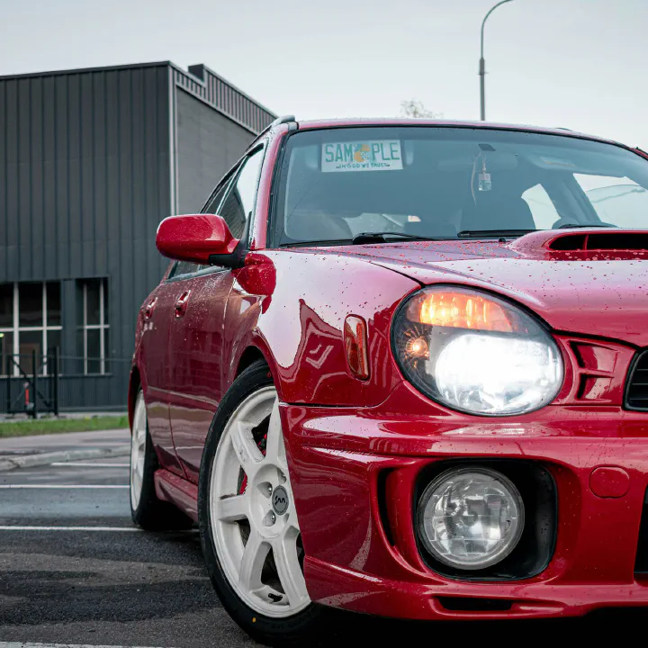 A red bugeye Subaru WRX with a sample plate behind the windshield.